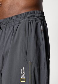 Pantaloni corti grigi scuri realizzati in tessuto leggero, con vita elastica, tasche, dettagli di cucitura gialla e logo del National Geographic.