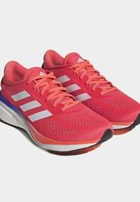 Zapatillas deportivas rojo brillante con parte superior de malla, acentos en rosa, tres rayas blancas y una suela acolchada con un diseño en degradado.