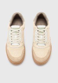 Sneaker beige con tessuto a rete, accenti in suede, suola in gomma e lacci bianchi piatti. Includono un'etichetta logo verde chiaro sulla linguetta.