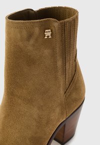 Stivale alla caviglia in suede marrone con pannelli elastici laterali, tacco in legno impilato e piccolo logo metallico sul lato esterno.