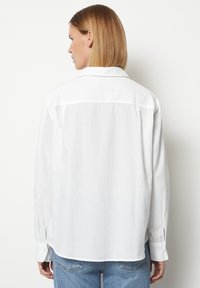 Weißes Langarmhemd aus leichtem Stoff, mit geradem Schnitt, geknöpften Manschetten und einem Rückenteil mit Yoke-Detail. Kombiniert mit heller Jeans.