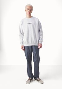 Sweatshirt gris avec le logo "VOLCOM" noir, coupe ample, poignets et ourlet côtelés. Assorti avec un pantalon bleu marine et des baskets beige-brun.