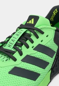 Chaussure de sport verte avec tige en mesh respirant, accents noirs et talon renforcé. Comprend l'étiquette "HEAT.RDY" et trois rayures noires.