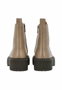 Botas de cuero hasta el tobillo en beige claro con un acabado suave, que cuentan con una suela de plataforma negra gruesa, cremallera trasera y un sutil detalle de costura.