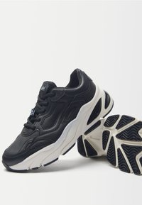 Sneakers in pelle nera con dettagli testurizzati, una suola intermedia bianca e una suola in gomma nera distintiva. Le caratteristiche di accento includono i lacci e il branding.