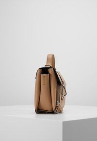 Beige kožená kabelka s texturovaným povrchem, s horním uchem, stříbrným kováním a otevřeným zipem. Kompaktní obdélníkový tvar.