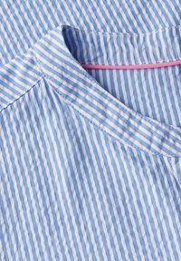 Blau-weißer gestreifter Stoff mit einer weichen Textur, der einen runden Ausschnitt und ein kontrastierendes pinkfarbenes Nähdetail am Kragen aufweist.