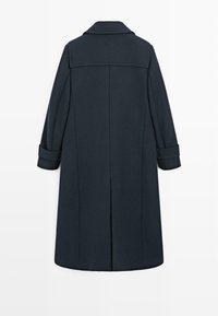 Cappotto lungo blu scuro realizzato in un misto lana. Presenta un collo con punte, maniche arrotolate, un taglio dritto e una fessura sul retro per facilitare i movimenti.