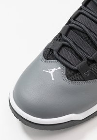 Szare skórzane sneakersy z czarnymi siateczkowymi akcentami, z szarymi sznurowadłami, białą podeszwą i małym białym logo Jumpman na palcu.