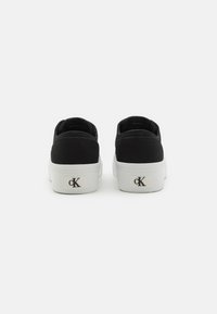 Sneakers negre din pânză cu talpă din cauciuc alb, având un detaliu cu logo pe călcâi, design simplu și fără accente sau modele vizibile.