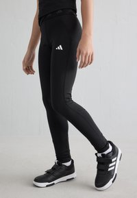Svarta sportleggings med hög midja, utrustade med vita logotypdetaljer. Kombinerat med svarta sneakers med två kardborreband.