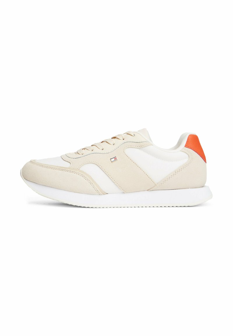 Scarpa sportiva beige con dettagli bianchi e un vivace tab del tallone arancione. Realizzata in pelle liscia e suede, presenta una suola testurizzata.