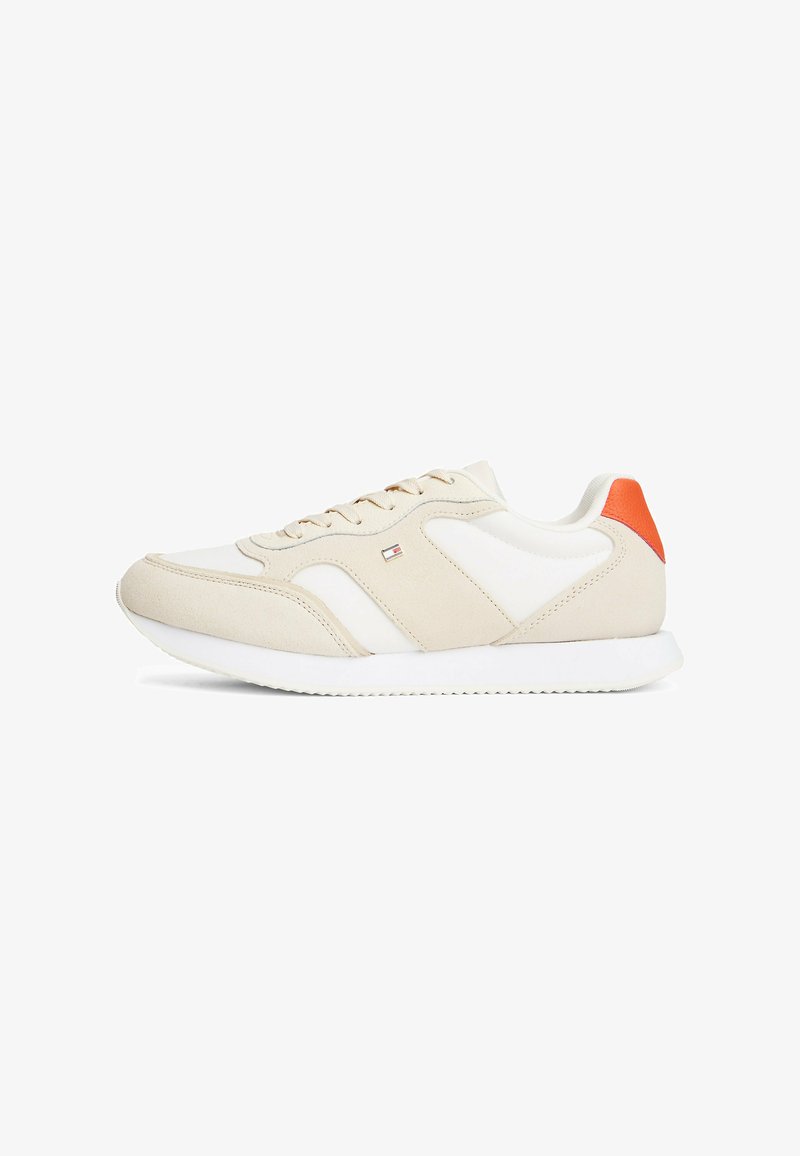 Scarpa sportiva beige con dettagli bianchi e un vivace tab del tallone arancione. Realizzata in pelle liscia e suede, presenta una suola testurizzata.