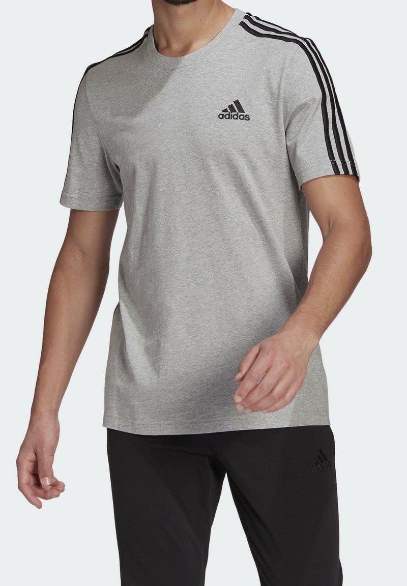 Camiseta gris de manga corta hecha de algodón, con acentos en negro de tres rayas en los hombros y un pequeño logo negro de Adidas en el pecho.