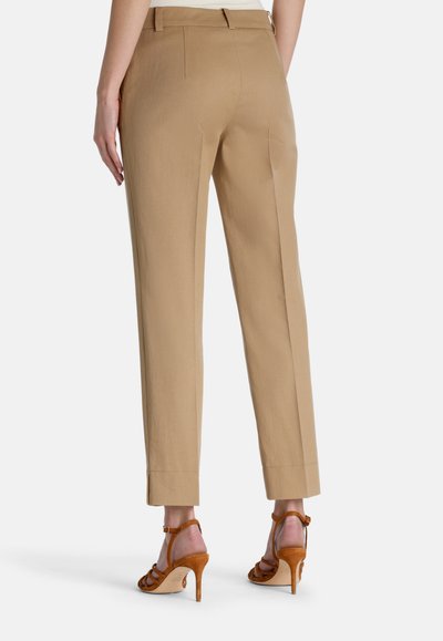 Beige housut, joissa on suora lahje, näyttävät puhtailta linjoilta ja minimaalilta saumoilta. Yhdistettynä ruskeisiin hihnakenkiin.