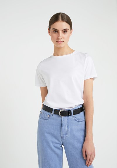 Camiseta blanca de manga corta combinada con jeans de tiro alto en un azul claro y un cinturón negro con una hebilla plateada, frente a un fondo liso.