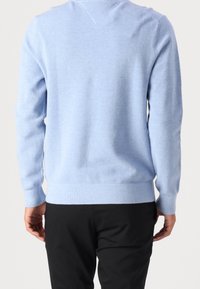 Hellblauer, strukturierter Pullover mit langen Ärmeln und einem V-Ausschnitt. Verfügt über einen gerippten Saum und Bündchen. Wird mit schwarzen Hosen getragen.