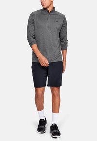 Grå langærmet trøje med kvart lynlås, letvægtsstof, parret med sorte shorts. Atletiske sko og hvide sokker fuldender outfittet.