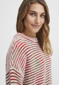 Stickad tröja med horisontella ränder i röd, rosa, beige och vit. Rund halsringning och textil med en lös passform.