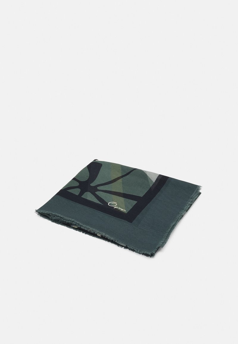 Foulard carré plié avec des motifs abstraits vert foncé, noir et bleu sarcelle atténué, bords effilochés sur un fond uni.