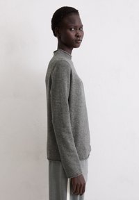 Grauer Pullover aus weichem Strickmaterial mit Stehkragen, langen Ärmeln und lockerer Passform. Strukturierte Oberfläche mit minimalen Details.