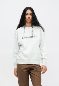 Jasnoszara bluza z logo "carhartt" w ciemniejszym odcieniu szarości, w luźnym kroju, z prążkowanymi mankietami i miękką fakturą, zestawiona z brązowymi spodniami.