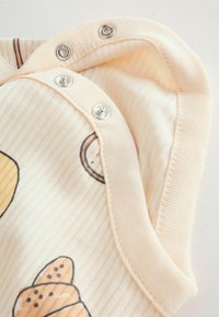 Világos őszibarack bordázott anyag nyomtatott péksütemény mintával; ezüst patenttal rögzíthető; puha tapintású, kontrasztos varrással.