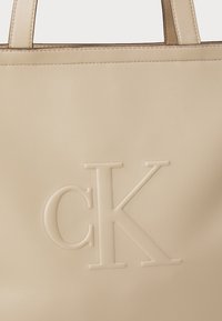 Bežna usnjena torba z embosiranim logotipom "CK", gladko teksturo in trdnimi ročaji. Preprost dizajn s čistimi črtami.