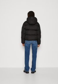 Schwarze Pufferjacke mit Kapuze, mit einem gesteppten Design. Kombiniert mit blauen Jeans, die einen lässigen Look abrunden.