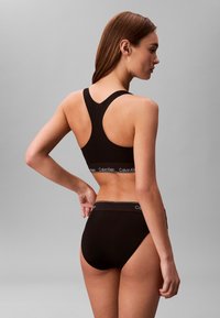 Czarny sportowy biustonosz o kroju racerback i marki elastycznej taśmy. Czarne majtki typu high-waist z prostą talią. Gładka faktura.