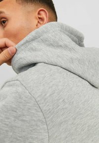 Sudadera con capucha gris de textura suave, mostrando un primer plano de la capucha y el escote. Detalles visibles de costuras y juntas.