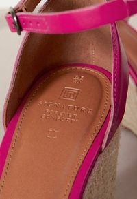 Jasnoróżowe sandały na paski z gładkiej skóry. Posiadają brązową wkładkę z wytłoczonym napisem „SIGNATURE FOREVER COMFORT” oraz plecioną koturnę.