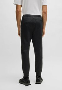 Svarta, åtsittande joggingbyxor med elastisk midja och bakficka, tillverkade av ett mjukt tyg med en subtil textur.