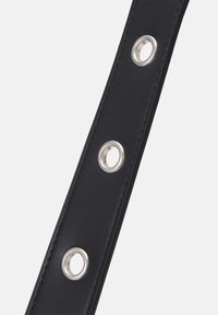Bracelet synthétique noir avec œillets en métal argenté, présentant une texture lisse et un design droit et étroit, adapté à divers accessoires.