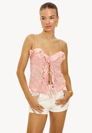 Roze paillettentop met een gerimpelde halslijn en spaghettibandjes, voorzien van een sluiting met een strik aan de voorkant en een aansluitende pasvorm. Gedirigeerd met witte shorts.