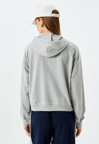 Grijze hoodie met brede mouwen, ribbelmanchetten en -zoom, van achteraf weergegeven. Gepaard met donkerblauwe broek, de stof lijkt zacht te zijn.