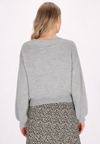 Pulover gri din tricot, cu o croială lejeră, tiv rib și mâneci lungi, expus peste o fustă cu model floral. Material texturat, respirabil.
