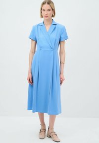 Robe légère bleu clair à manches courtes avec un design col, un devant enroulé et des plis. Comprend deux boutons à la taille.
