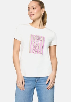 Femme aux cheveux châtain clair portant un t-shirt blanc avec un motif rayé rose et le texte "Ciao for Now!" au-dessus d'une voiture, assorti à un jean bleu.
