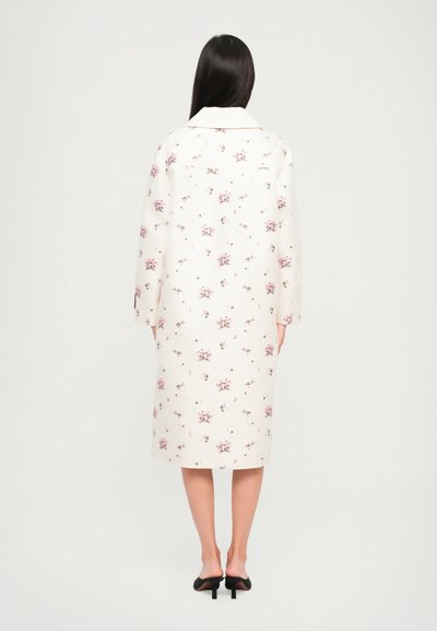 Virágmintás, törtfehér kabát hosszú ujjakkal, kivágott gallérral és egyenes fazonnal. Közepes hosszúságú, puha tapintású.