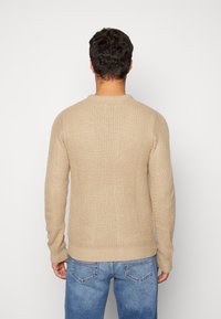 Beige neulepaita, jossa on tekstuuri ja kudottu kuvio. Ominaisuuksiin kuuluvat pitkät hihat, pyöreä pääntie sekä ribbireunat hihoissa ja helmassa. Rentosovitus.