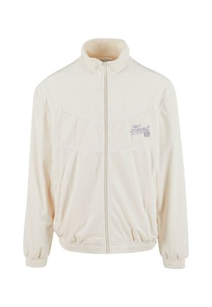 Cremefarbene Trainingsjacke mit hohem Kragen, Frontreißverschluss und elastischen Bündchen. Verfügt über weiße Nähte und ein kleines Logo auf der Brust.