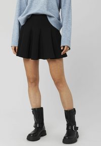Jupe plissée noire avec un design évasé. Associée à un pull en tricot bleu clair. Bottines noires avec des accents à boucle et une finition texturée.