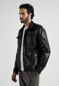 Schwarze Lederjacke mit einem Reißverschluss vorne, zwei Brusttaschen und seitlichen Reißverschlusstaschen. Sie hat einen Stehkragen und ein tailliertes Design.
