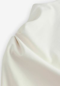 Tissu de couleur crème avec une texture lisse, présentant des plis et un drapé délicat. Aucun motif ou accent visible. Matière douce et légère.