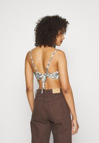 Bralette floral com alças finas, atado nas costas. Combinado com jeans de perna larga castanho escuro de cintura alta, com um rótulo na cintura.