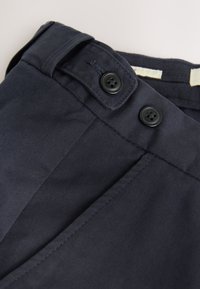 Tissu bleu marine à texture lisse, avec deux boutons noirs et un détail de ceinture rabattue.