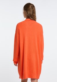 Oversized orange stickad klänning med långa ärmar, gjord av mjukt, fluffigt material, med en avslappnad passform och ribbade fållar och ärmslut.