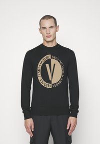 Zwarte gebreide trui met een ronde halslijn, met een groot beige Versace logo-ontwerp op het midden. Geribbelde manchetten en zoom.