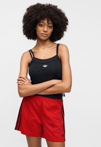 Μαύρο αμάνικο τοπ με δύο ράντες και μικρό λευκό λογότυπο, σε συνδυασμό με κόκκινα σορτς με μαύρες πλευρικές ρίγες και ελαστική μέση.